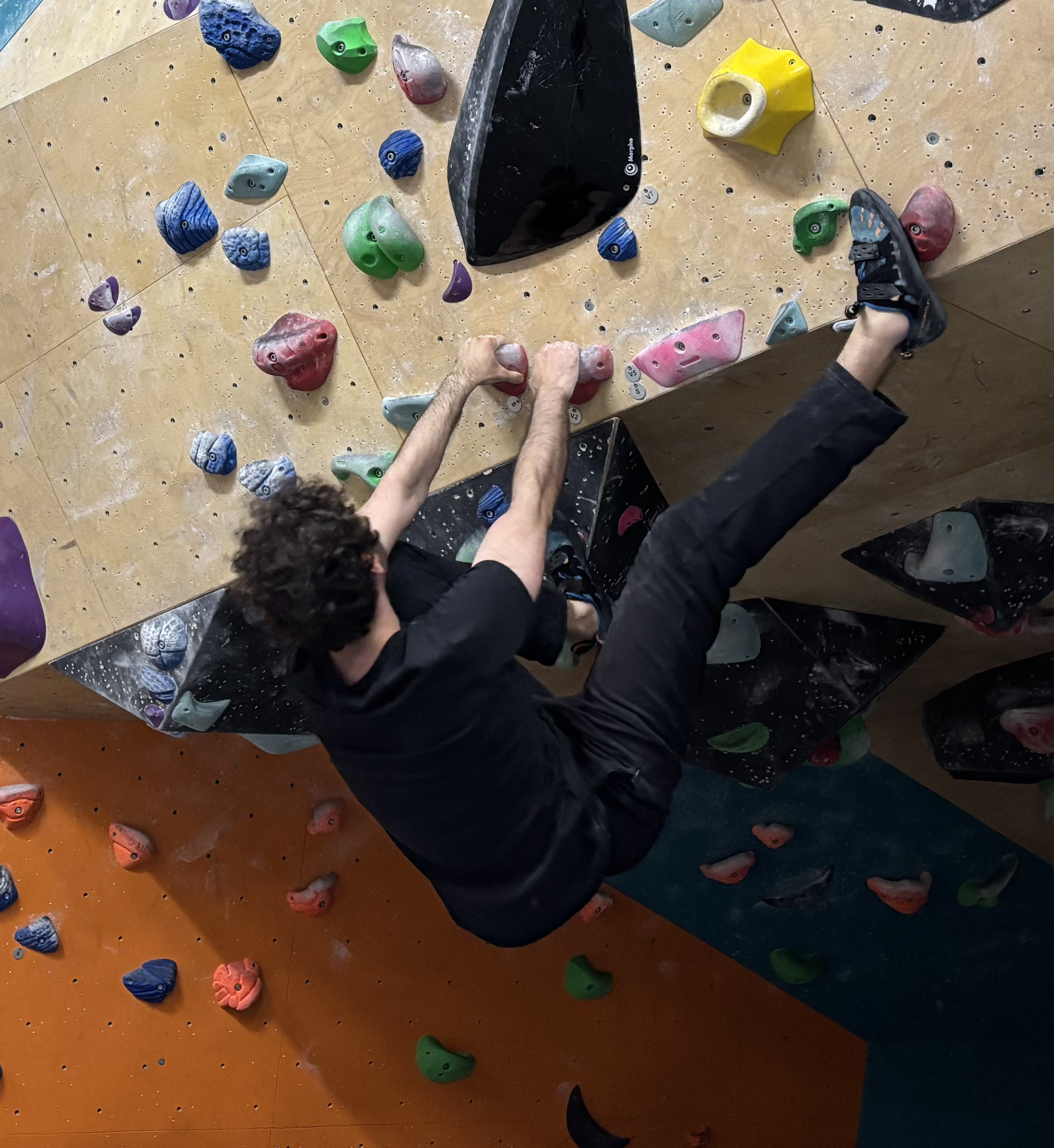 Doğukan stretched across a steep indoor bouldering wall.