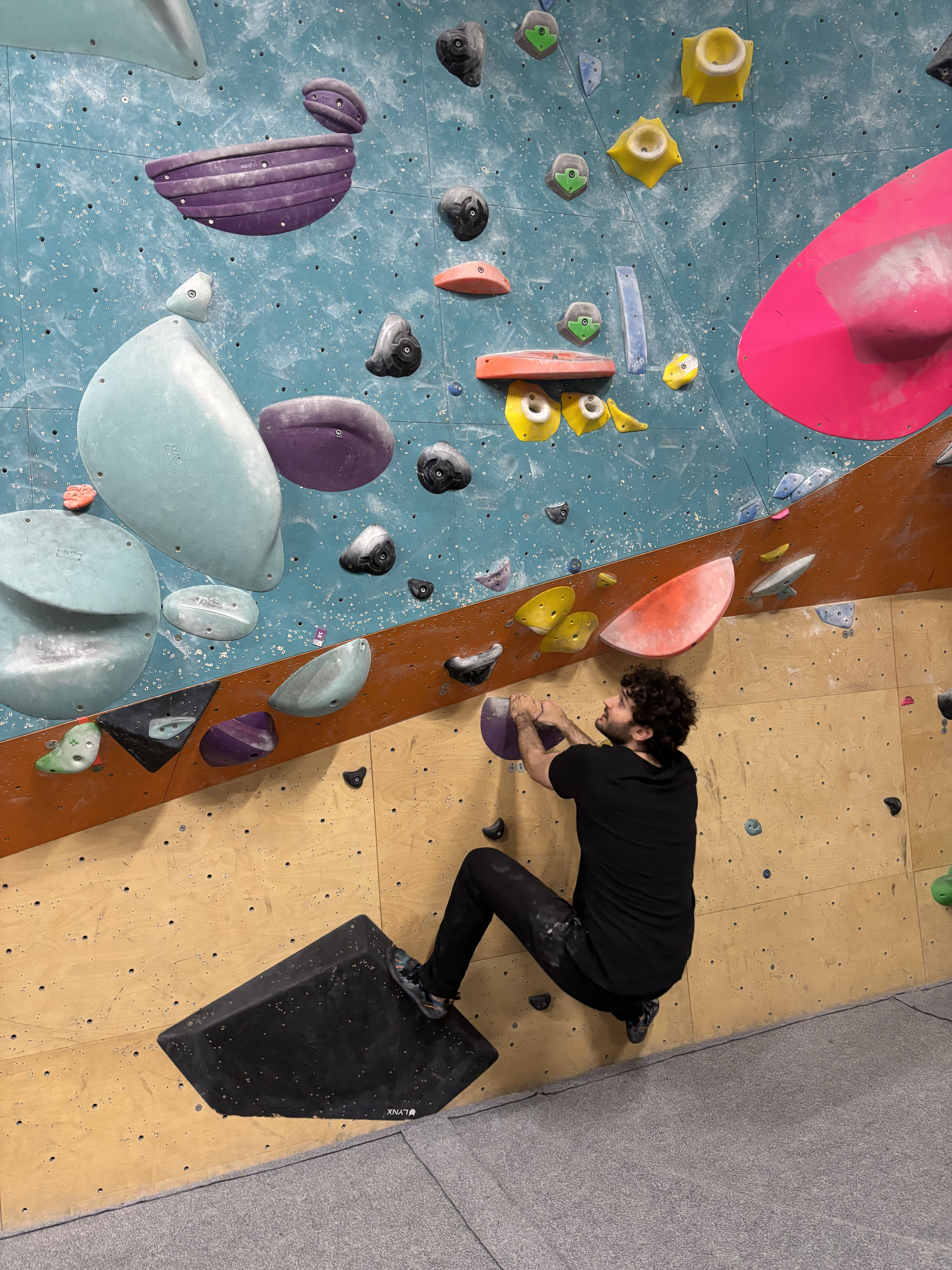 Doğukan sitting under a bouldering wall at the start of a route.